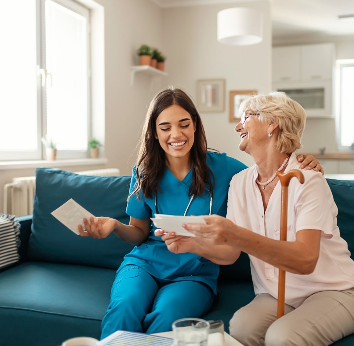 Caregiver Spending Quality Time with Senior at Home Caregiver and elderly woman sitting on a couch smiling and reviewing papers together in a warm and inviting living room.