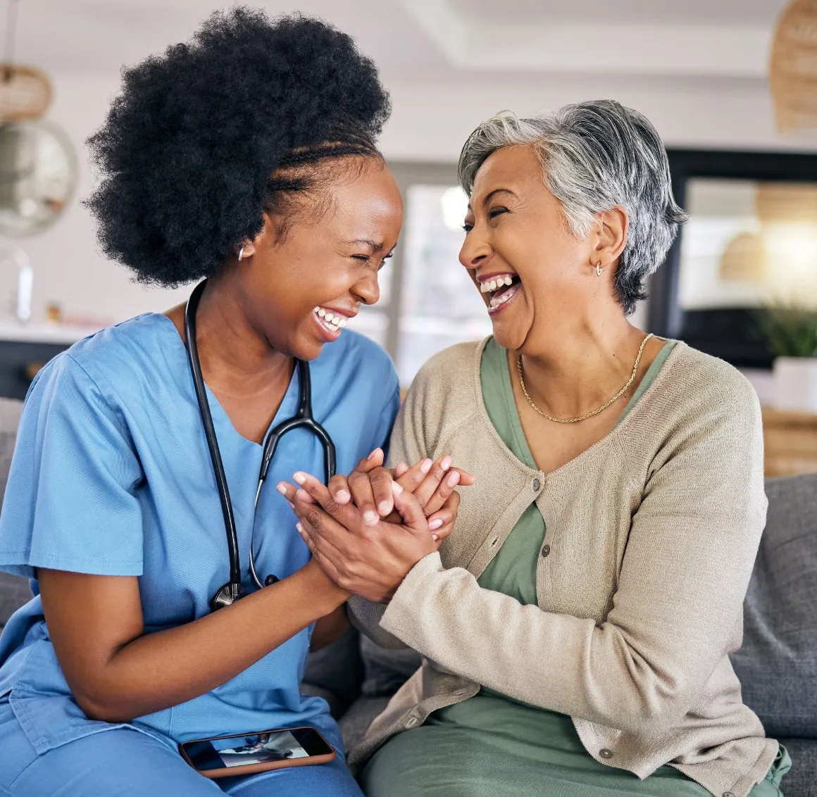Caregiver and senior laughing holding hands on sofa